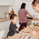 Father and child enjoy bonding over music in a cozy modern kitchen setting.